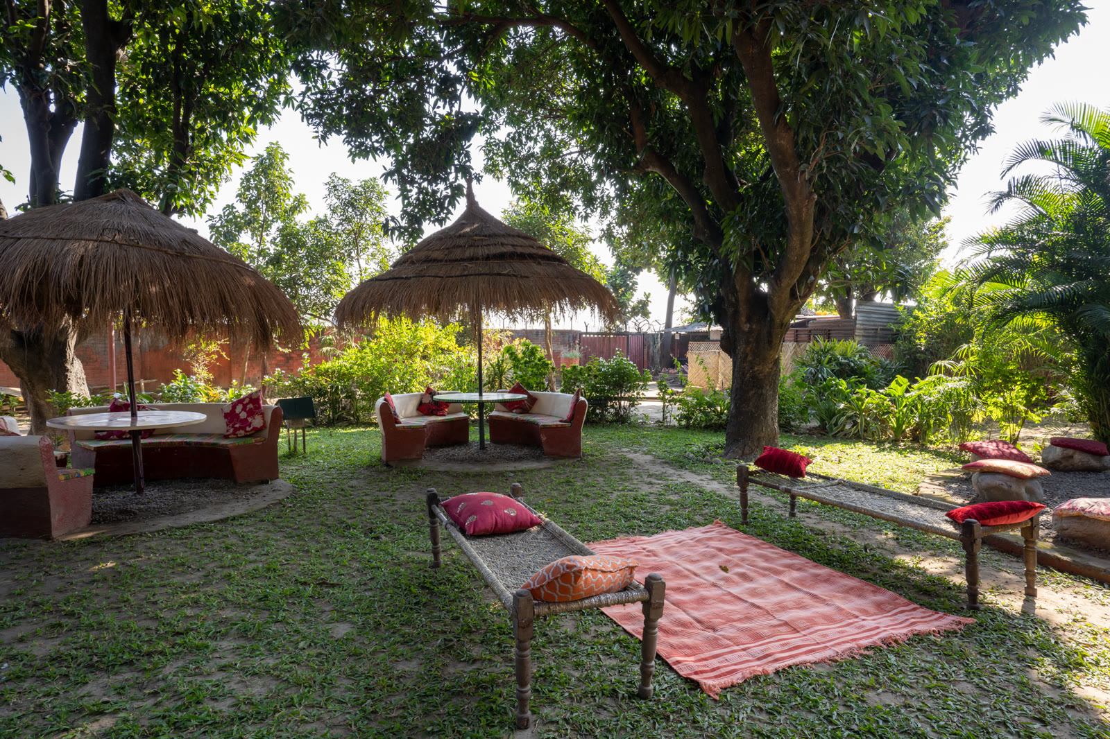 Charpais, cushions and thatched shades under the trees at the Baradari