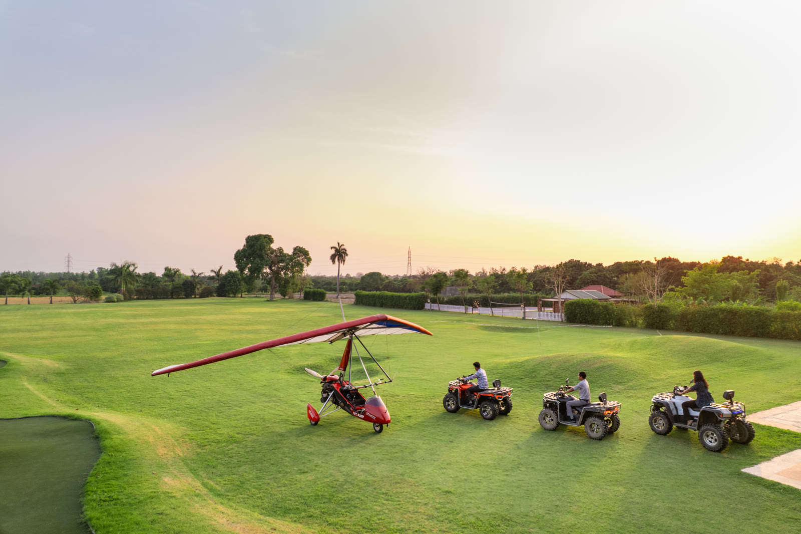 An ultralight trike and three ATVs on the grass at sunset